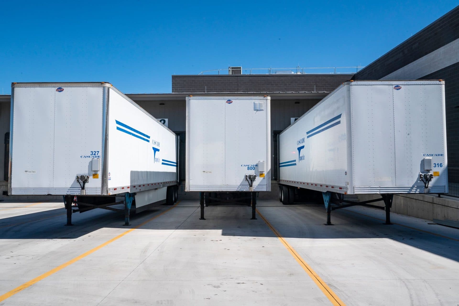 Three white dry van trailers backed into warehouse loading docks