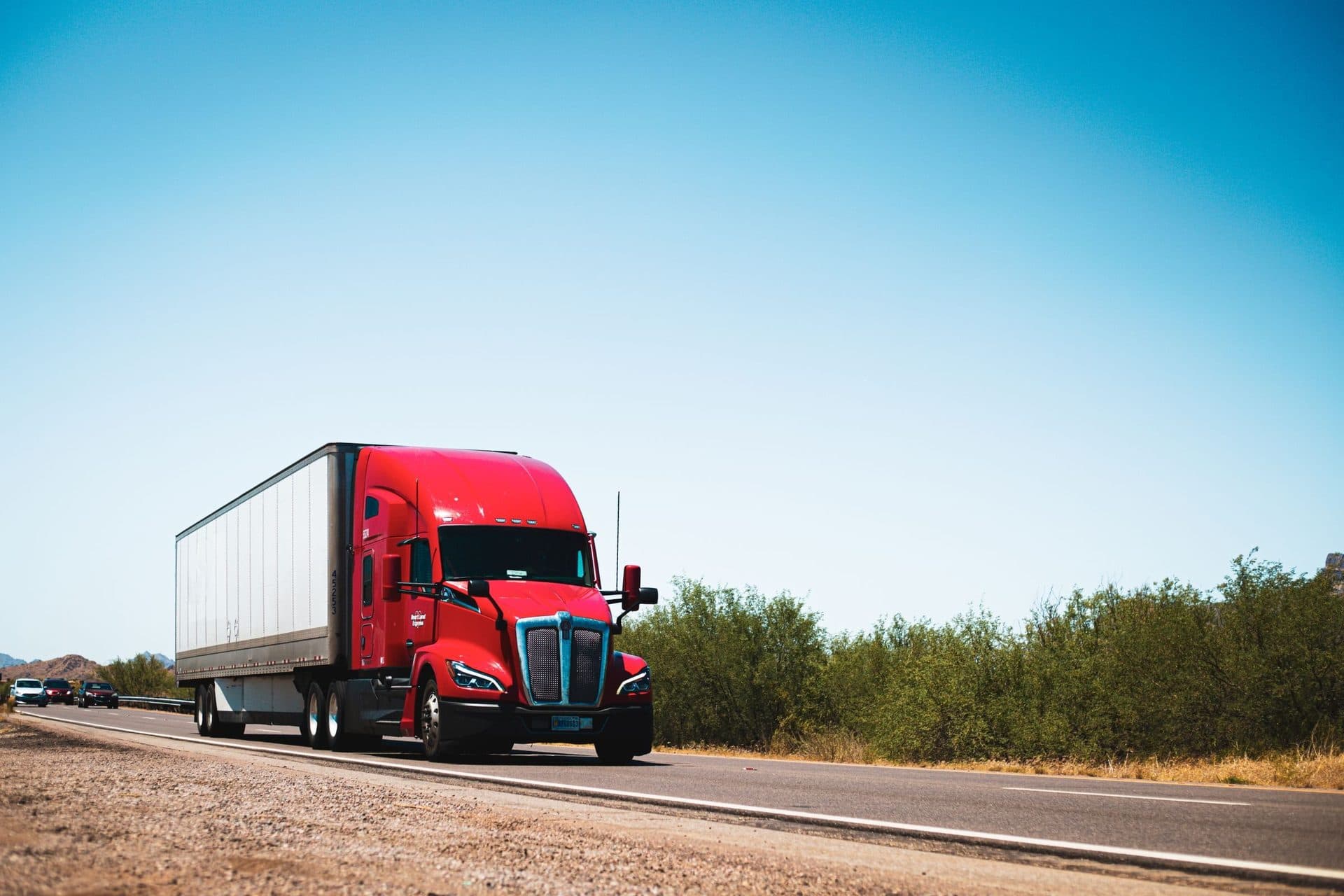 Red day-cab tractor pulling a white 53-foot dry van on an open two-lane highway
