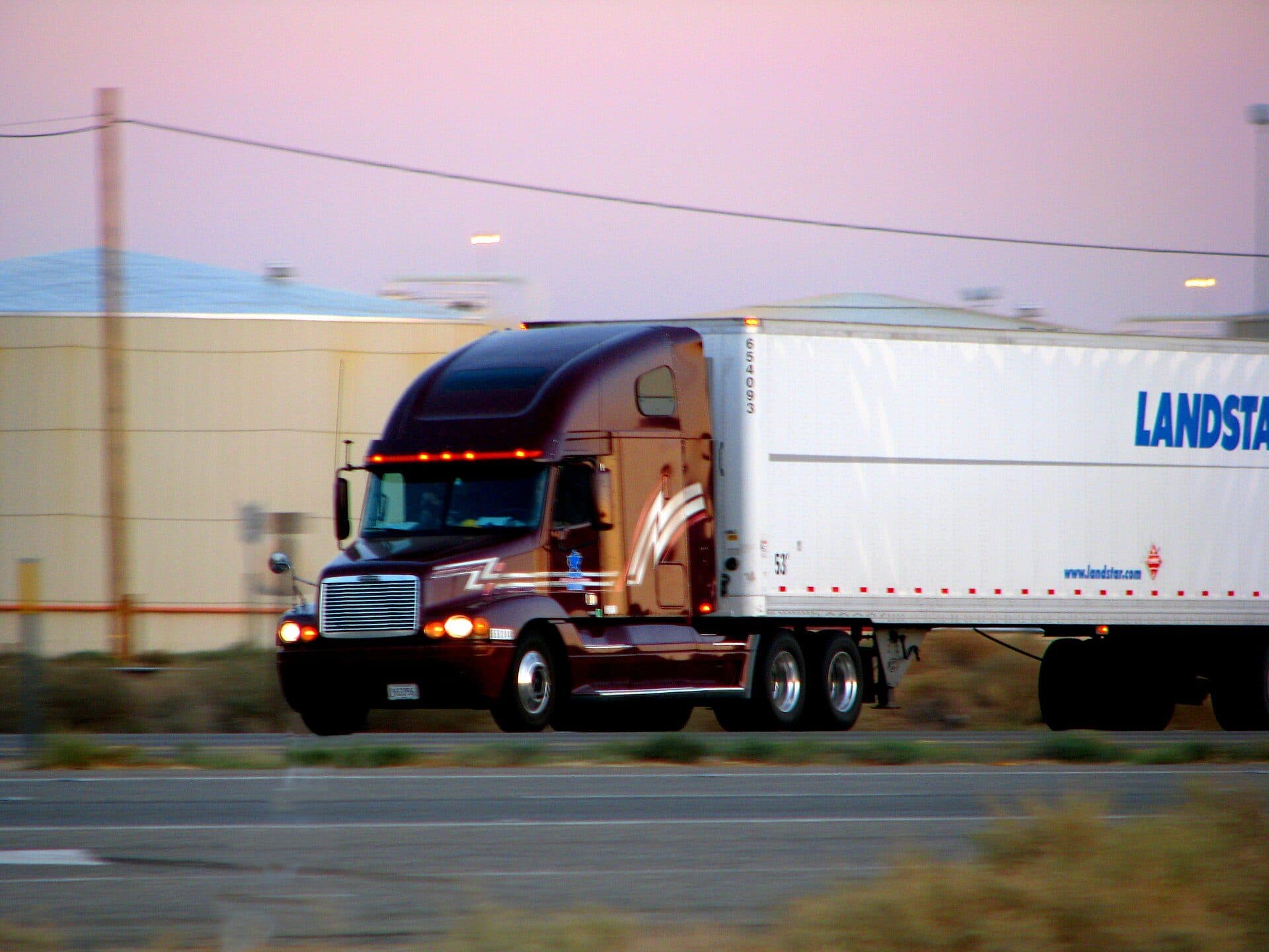 Dark blue conventional tractor hauling a white Landstar dry van at speed