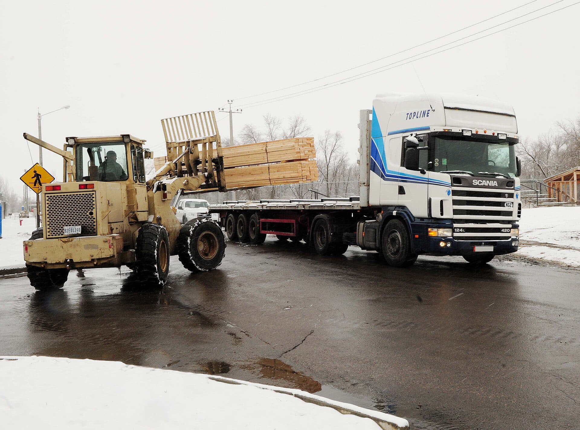 Forklift loading lumber onto a flatbed trailer in winter
