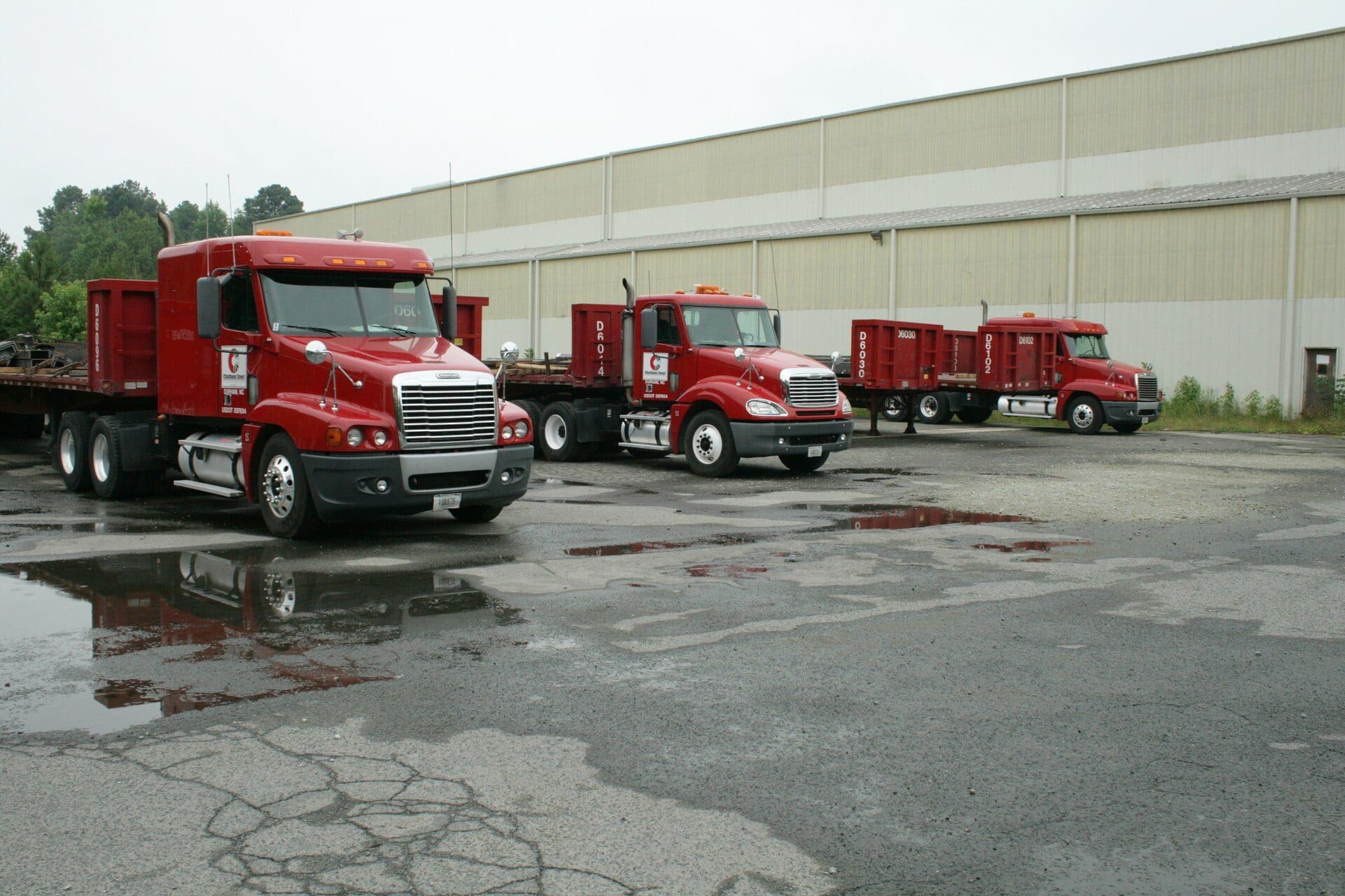 Row of red tractors with flatbed trailers parked at a yard