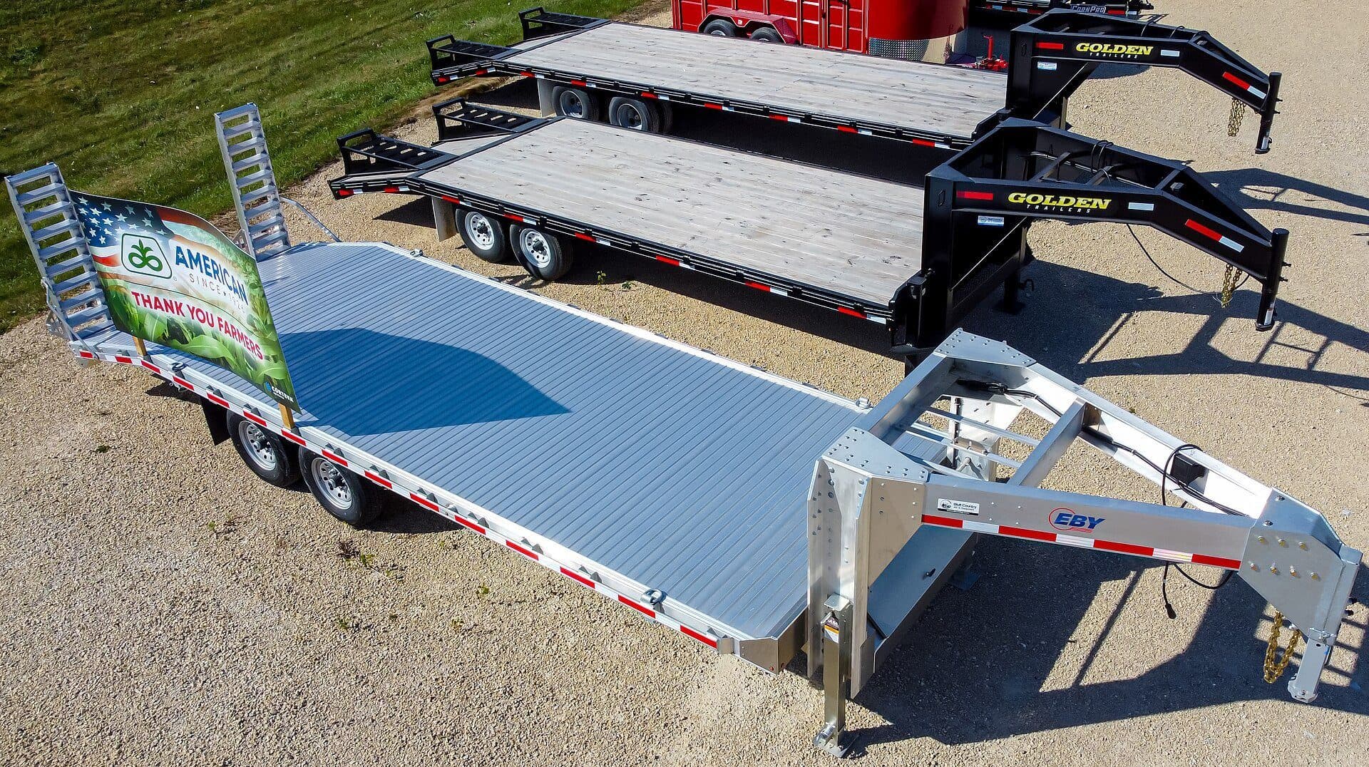 Gooseneck deckover trailers and an aluminum equipment trailer lined up on a dealer lot