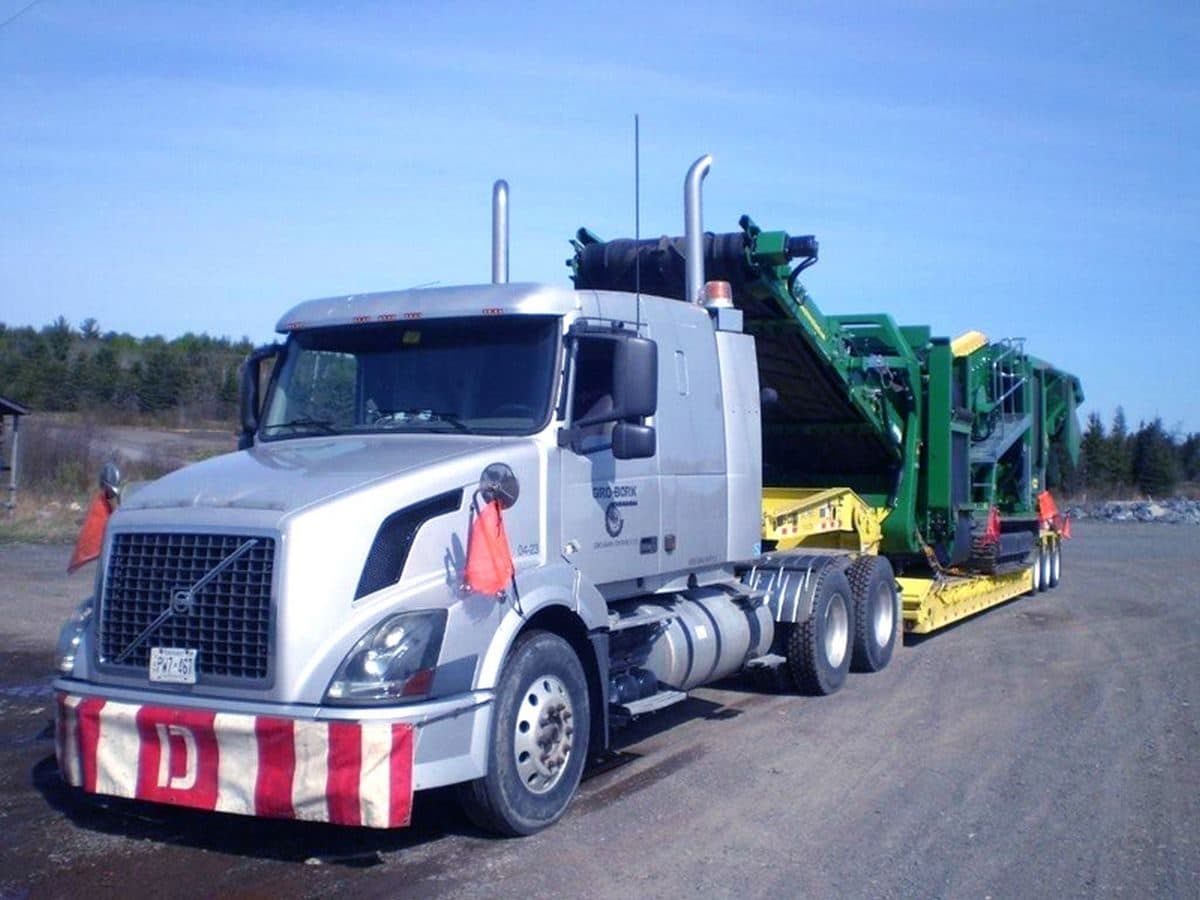 Volvo tractor coupled to a removable-gooseneck lowboy carrying green equipment