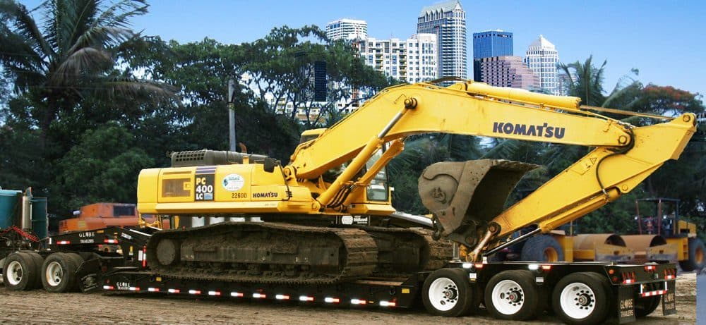 Detachable-gooseneck lowboy trailer carrying a yellow excavator