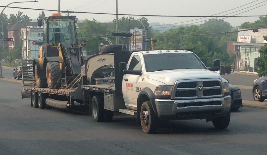 Ram 5500 cab-chassis towing a gooseneck flatbed loaded with a compact wheel loader