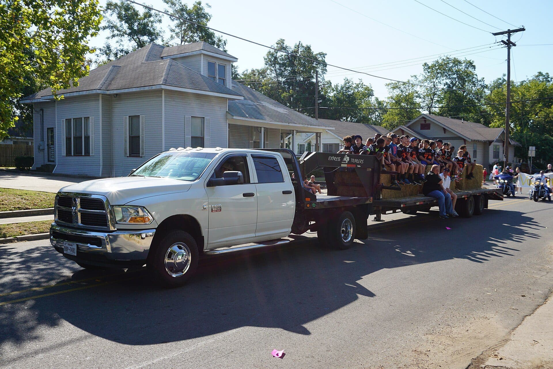 White Ram dually towing a loaded flatbed trailer down a residential street