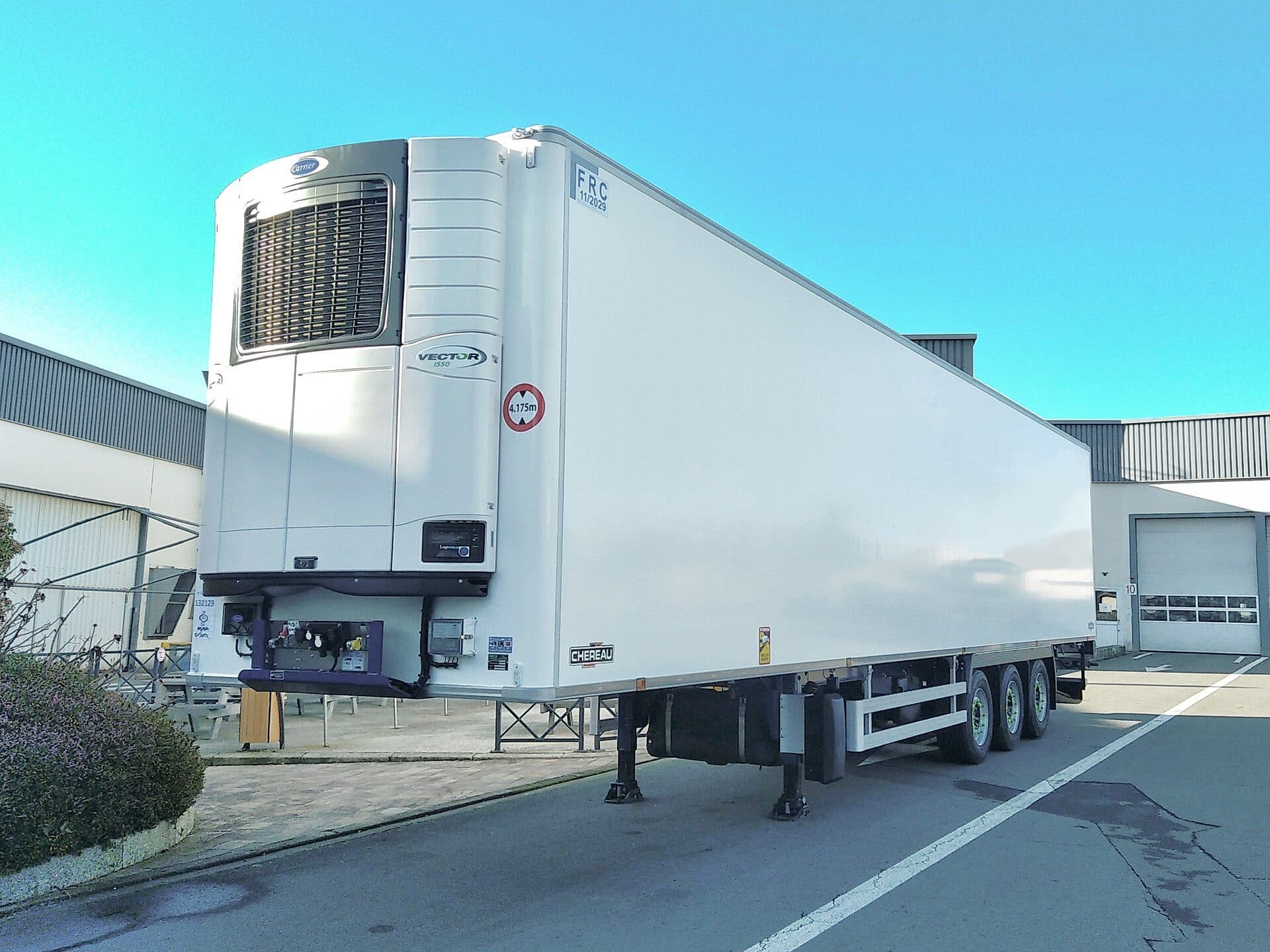 White refrigerated semi-trailer with a nose-mounted refrigeration unit parked outside a depot