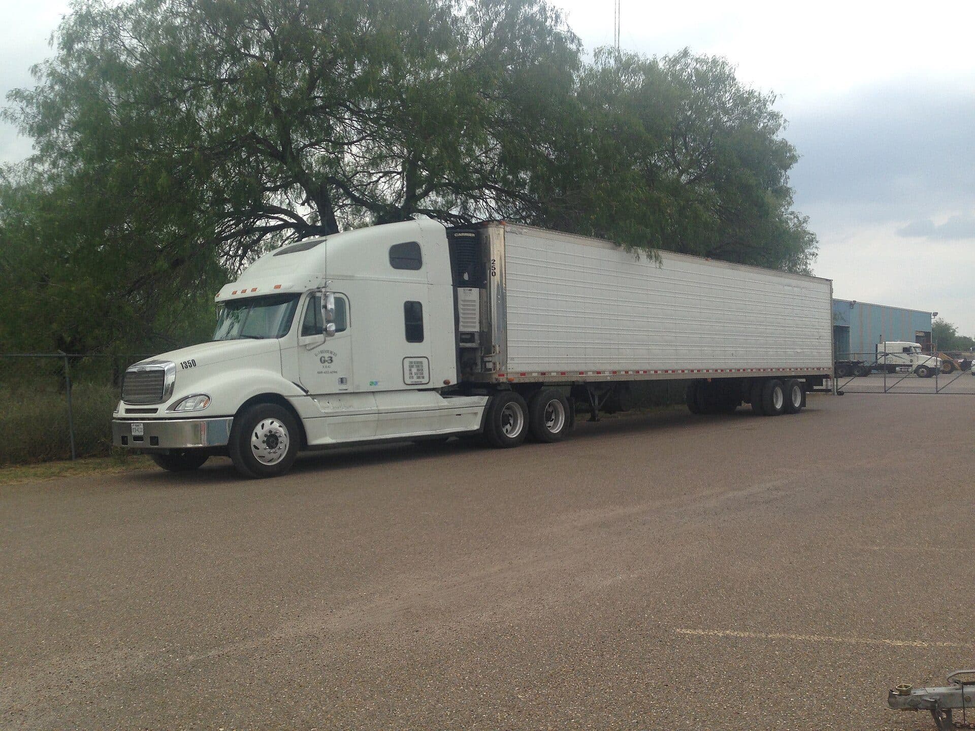 White sleeper tractor with a refrigerated trailer parked in a gravel lot