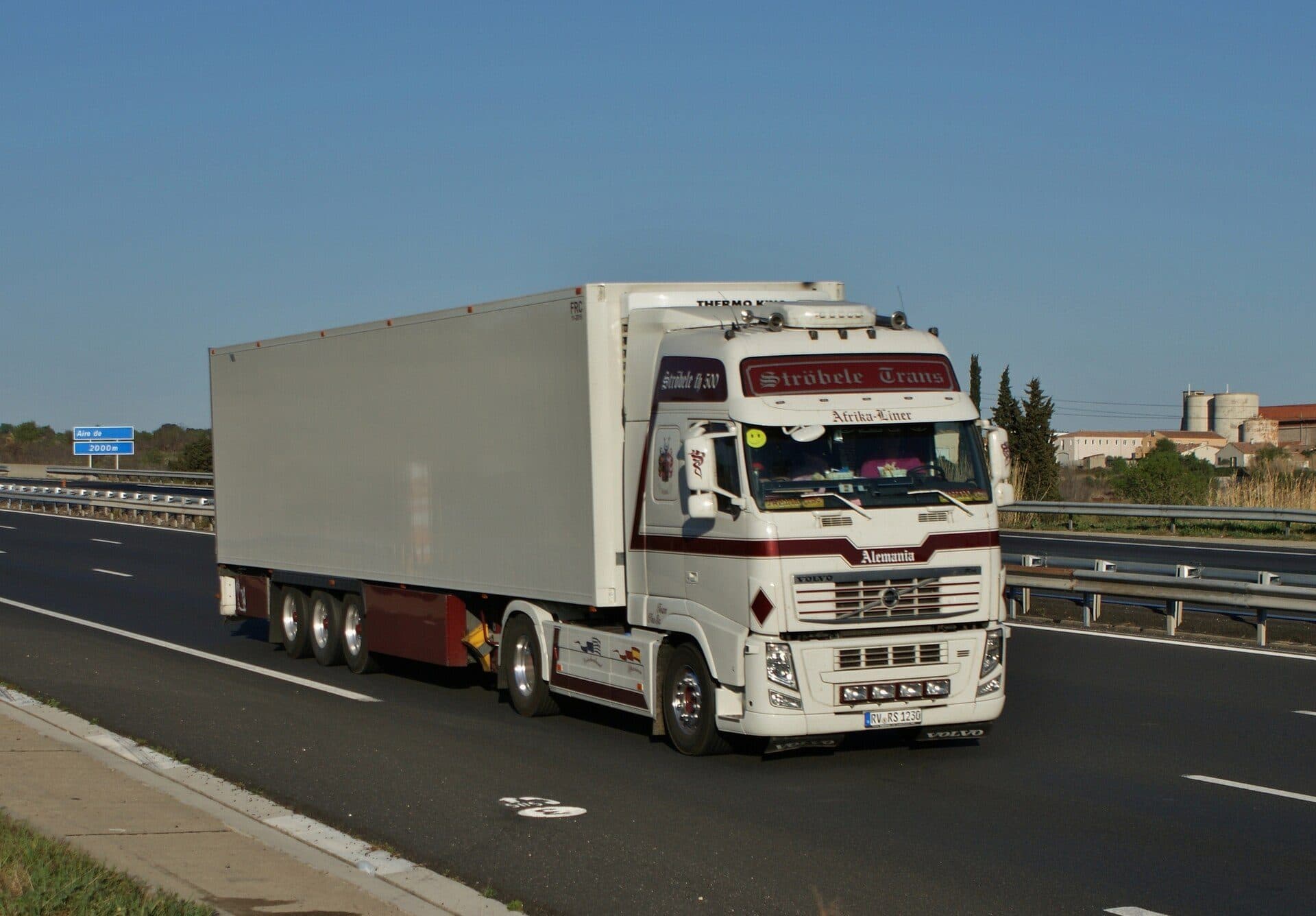 White Volvo tractor hauling a refrigerated trailer on a divided highway